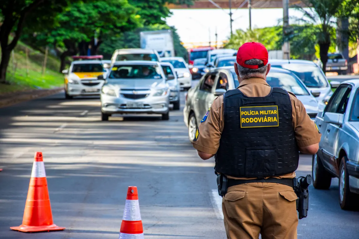 Agente da Polícia Rodoviária Militar orientando o trânsito em via com cones de sinalização