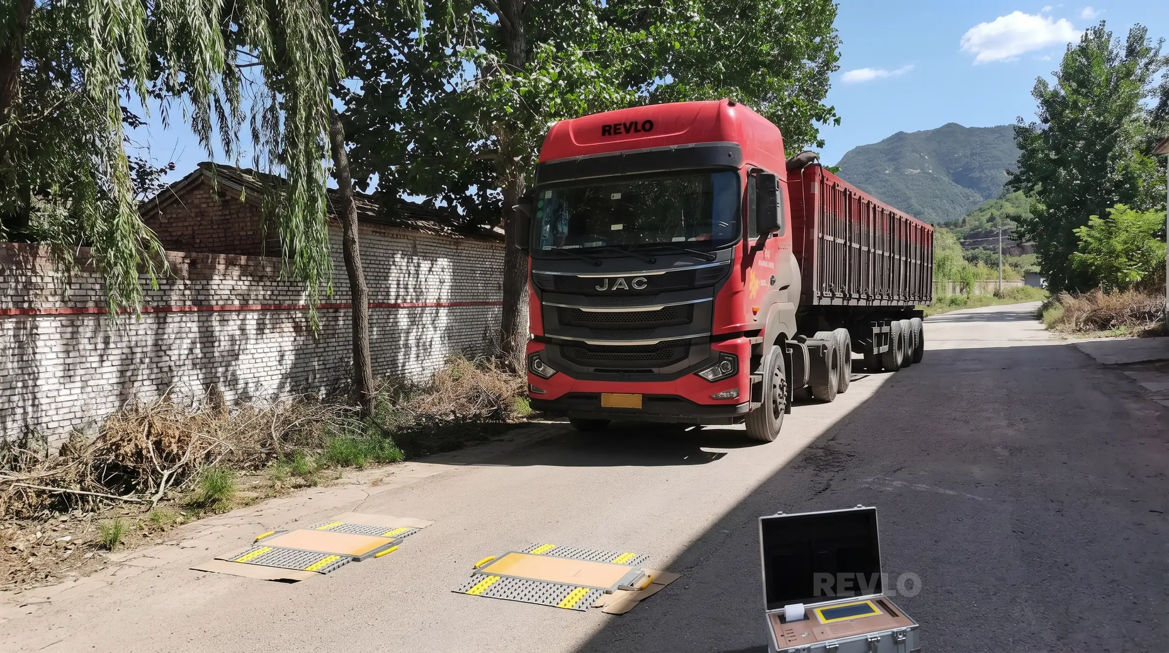 Caminhão com carreta basculante parado sobre as plataformas da balança Revlo, com a maleta do display aberta no chão ao lado