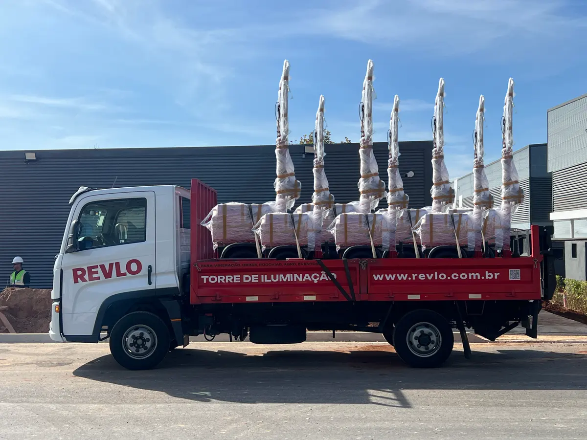 Caminhão da Revlo carregado com sete torres de iluminação embaladas, saindo da fábrica para entrega