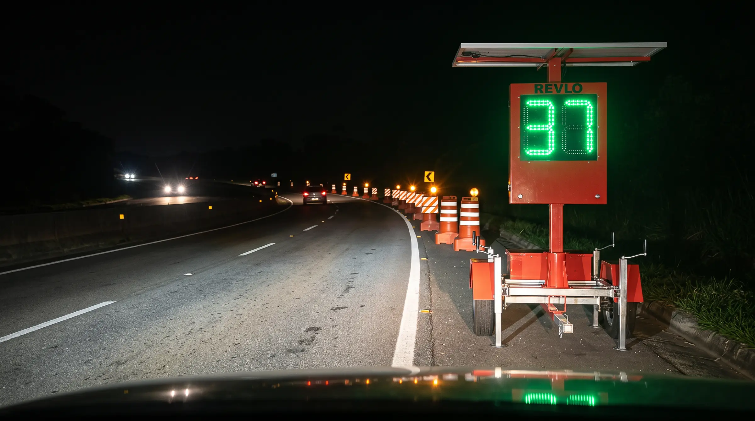Lombada eletrônica móvel Revlo à noite na beira de uma rodovia, antes de um desvio provisório com barreiras listradas, mostrando 37 em LED verde