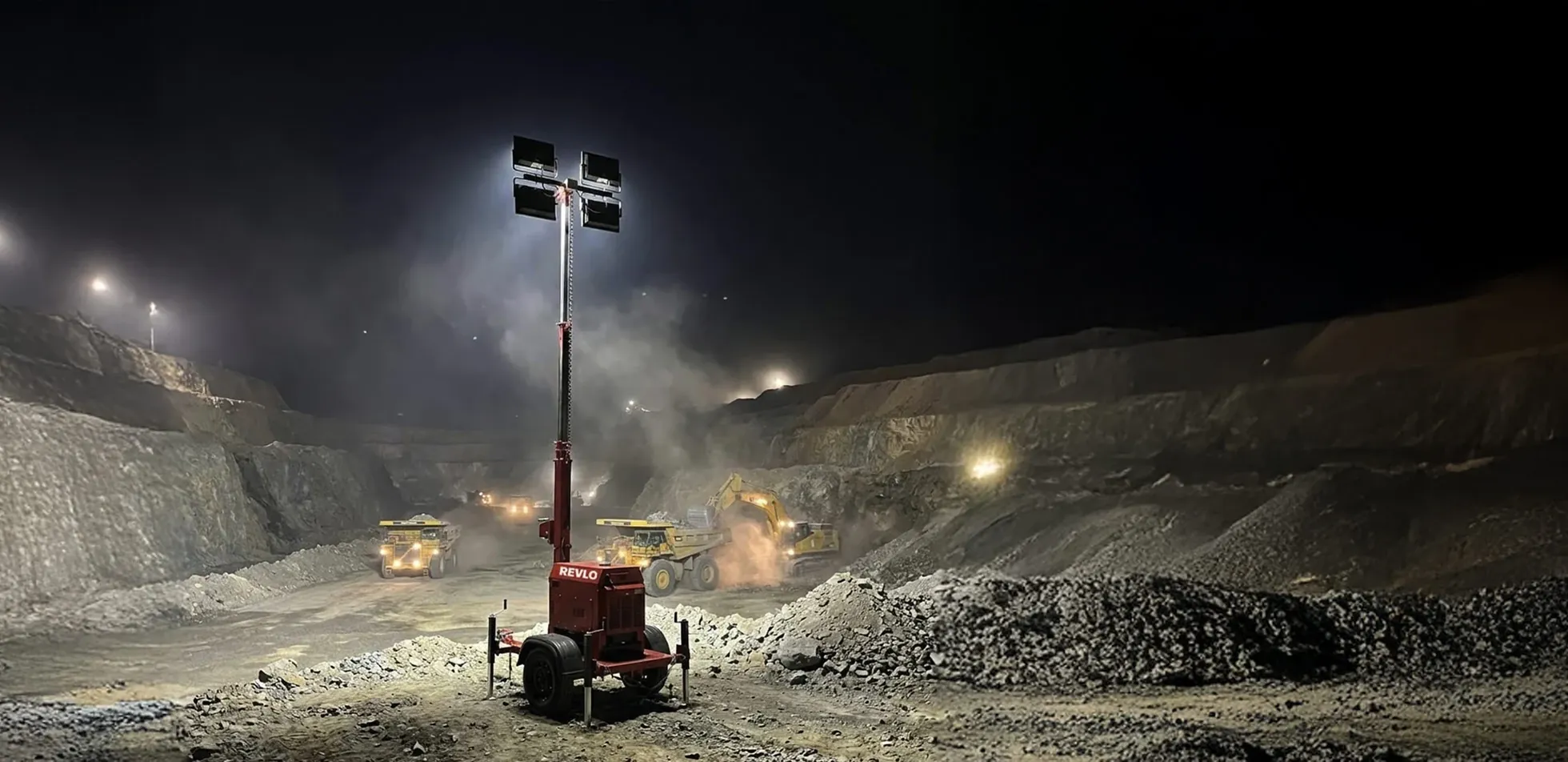 Torre de iluminação Revlo iluminando uma cava de mineração à noite, com caminhões fora de estrada e escavadeira em operação
