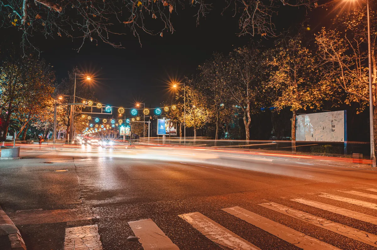 Avenida à noite com faixa de pedestres e rastros de luz de veículos