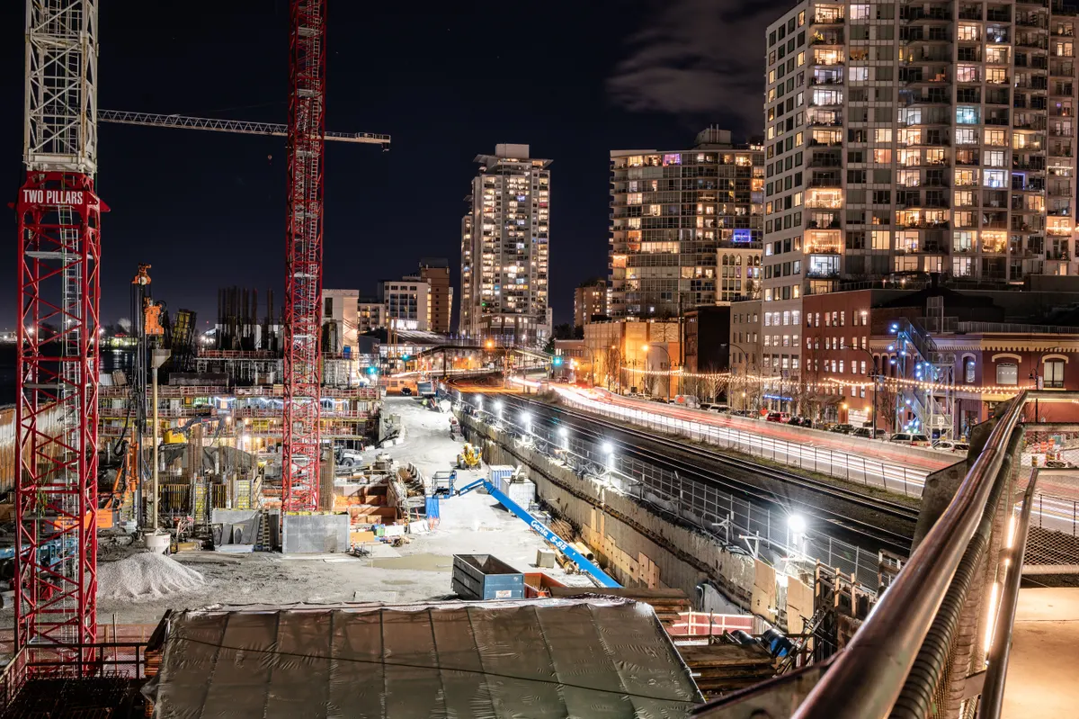 Canteiro de obras cercado por vias movimentadas e prédios, fotografado à noite