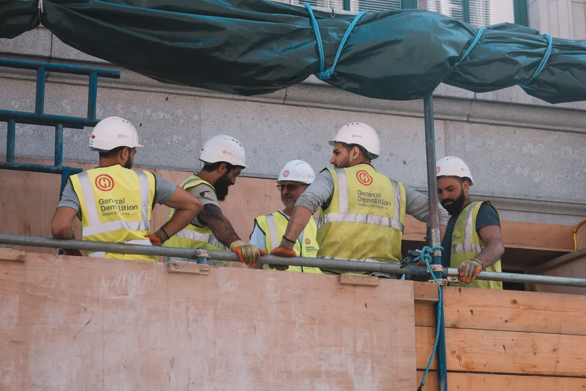 Grupo de trabalhadores de capacete branco e colete reunidos em obra