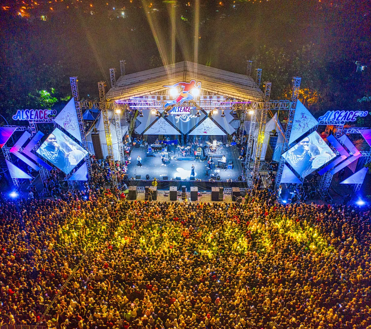 Vista aérea de palco de festival iluminado com grande público em frente