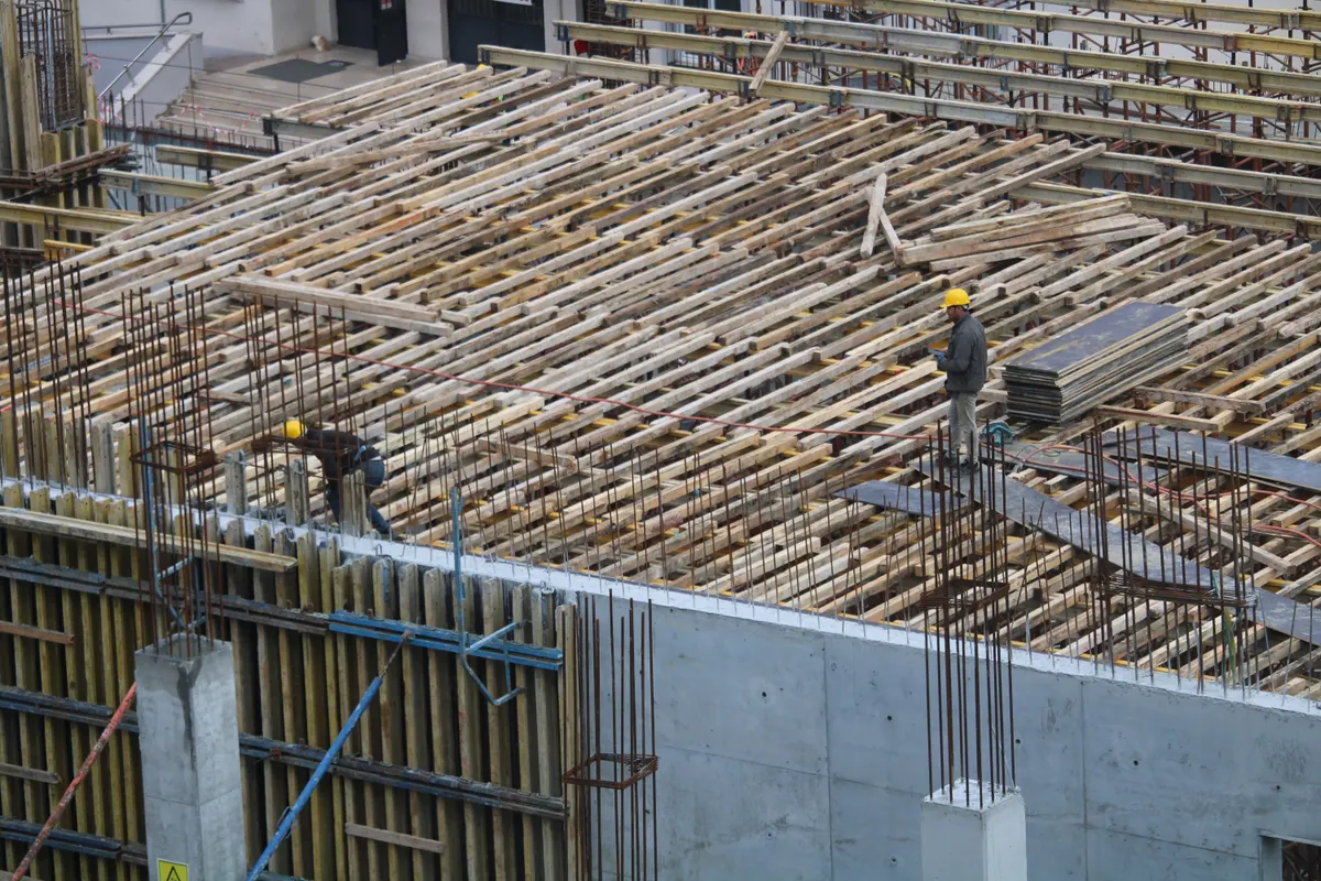 Operários trabalhando sobre laje com armadura de ferro montada, vista em perspectiva