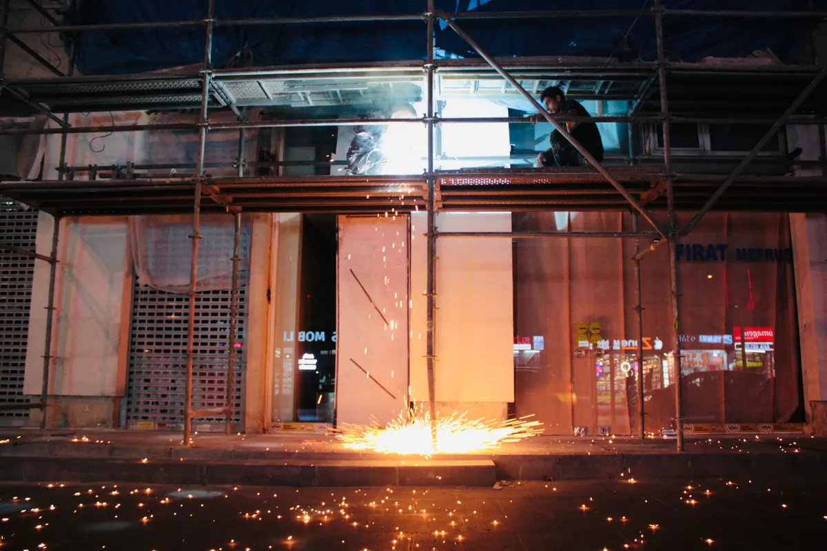 Fachada de edifício em obras à noite com faíscas de solda caindo sobre o piso