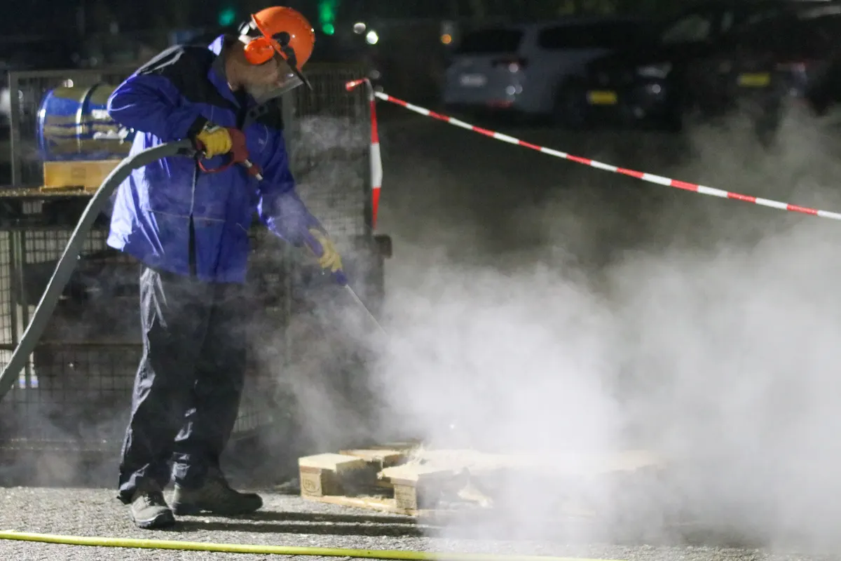 Operário lavando o pavimento com jato de alta pressão à noite, cercado por vapor