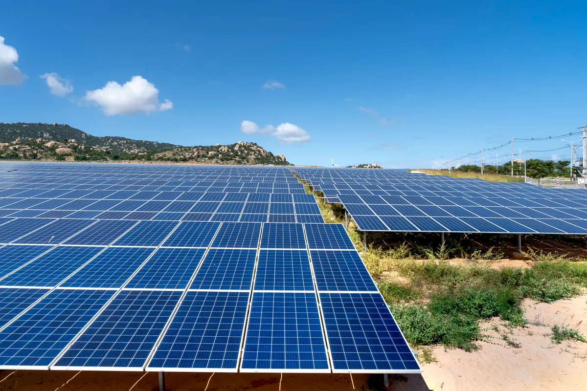 Painéis solares fotografados de baixo contra céu azul com nuvens