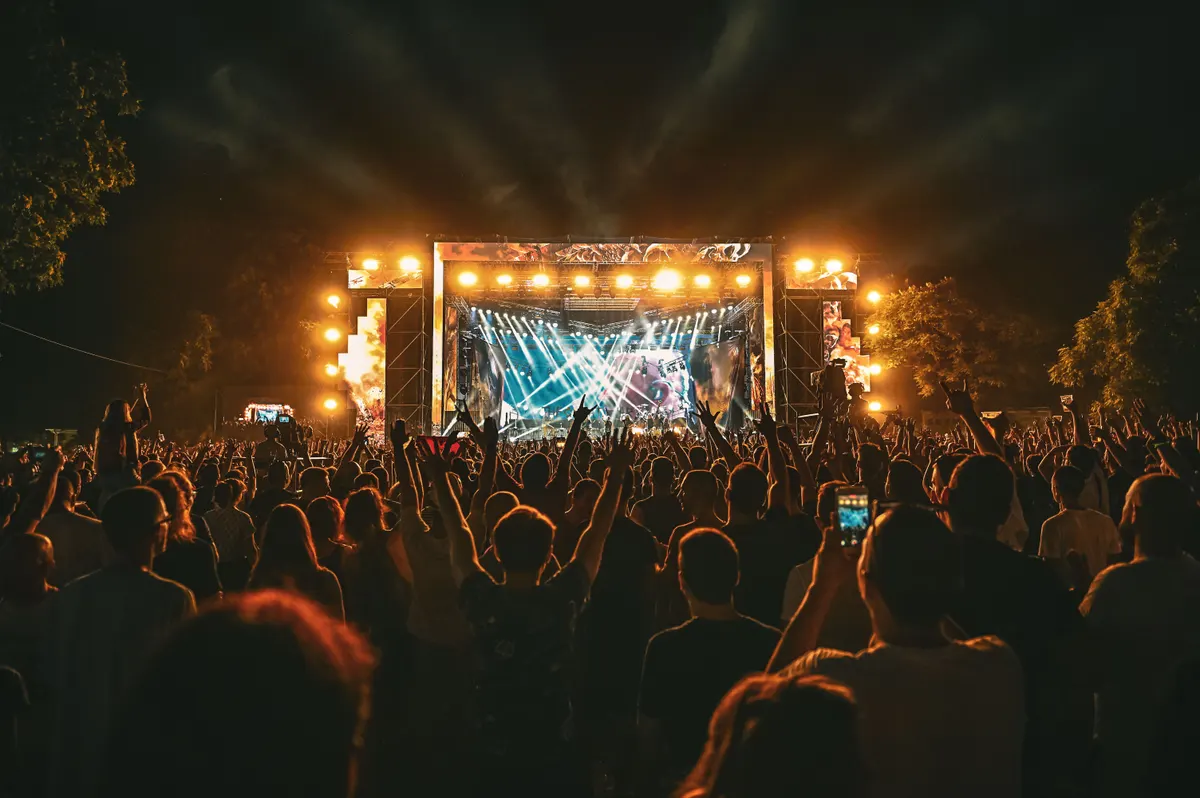 Palco ao ar livre iluminado à noite com público em silhueta