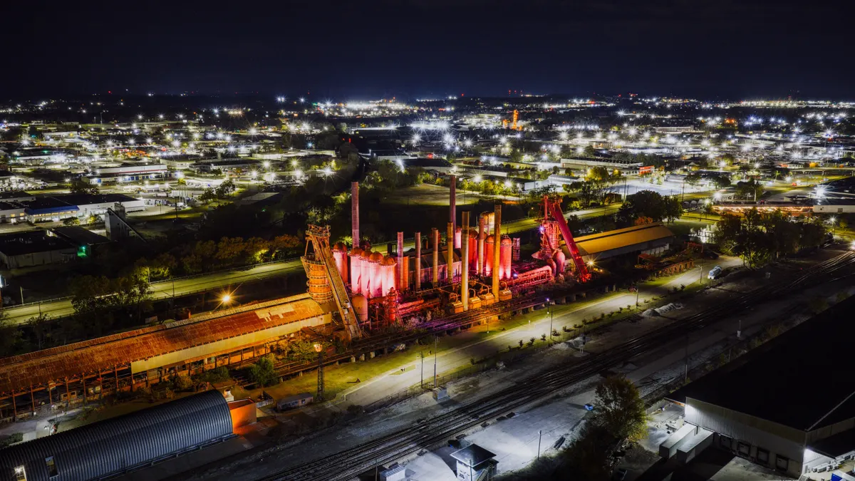Vista aérea noturna de pátio industrial com maquinário pesado e vias iluminadas