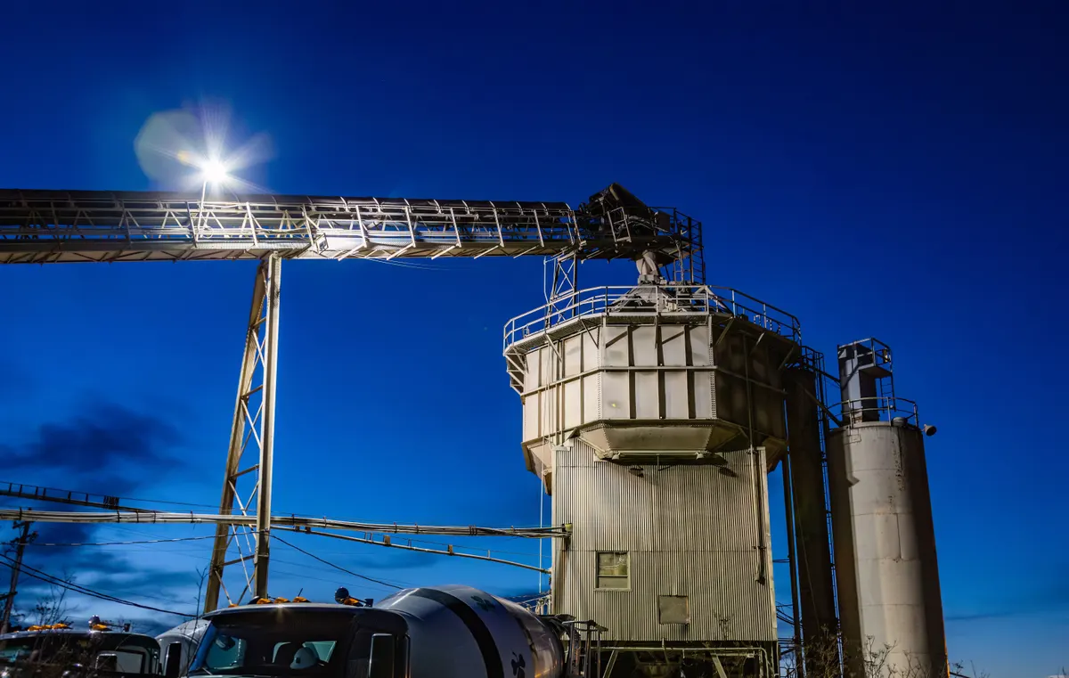 Silo e pórtico metálico de central de concreto iluminados contra o céu do fim de tarde