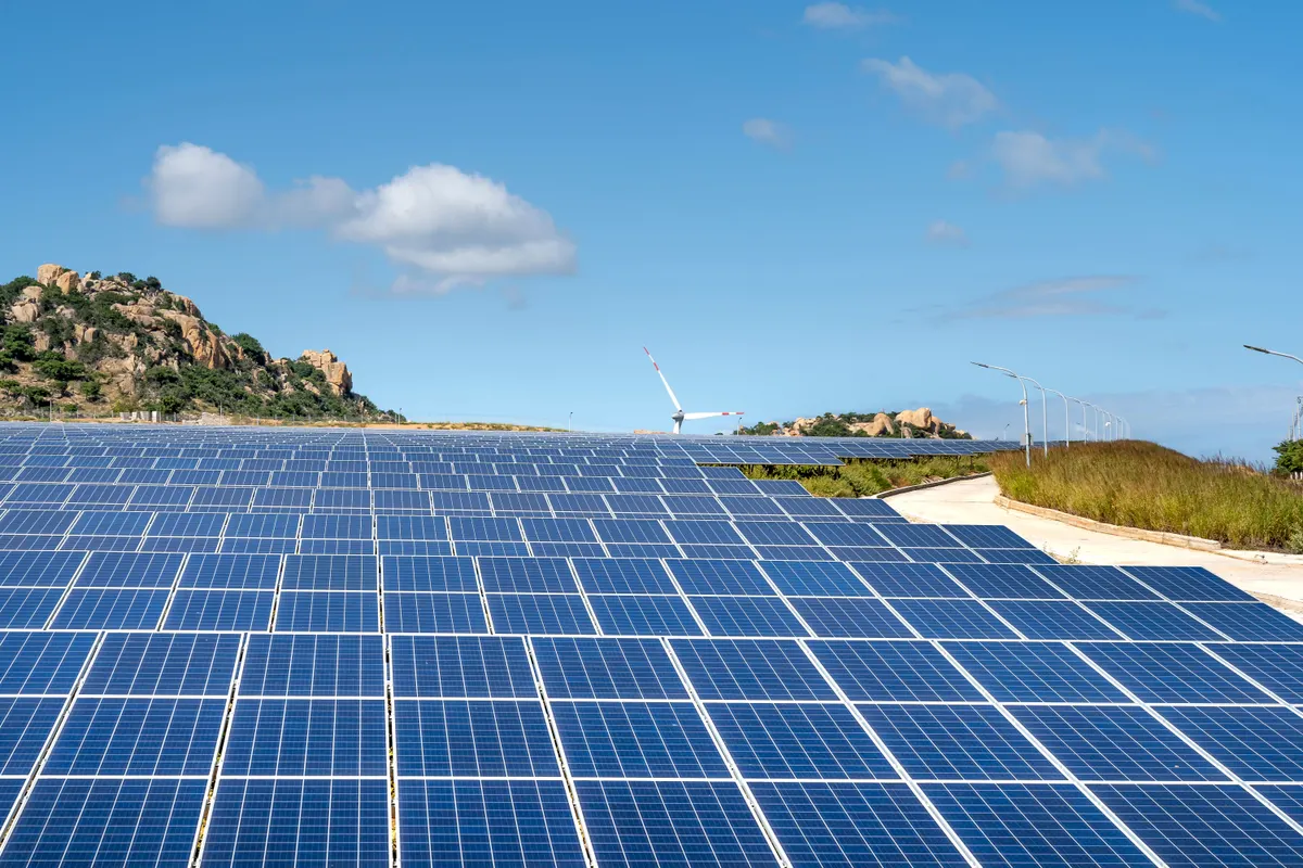 Painéis solares instalados em encosta, com torres eólicas ao fundo