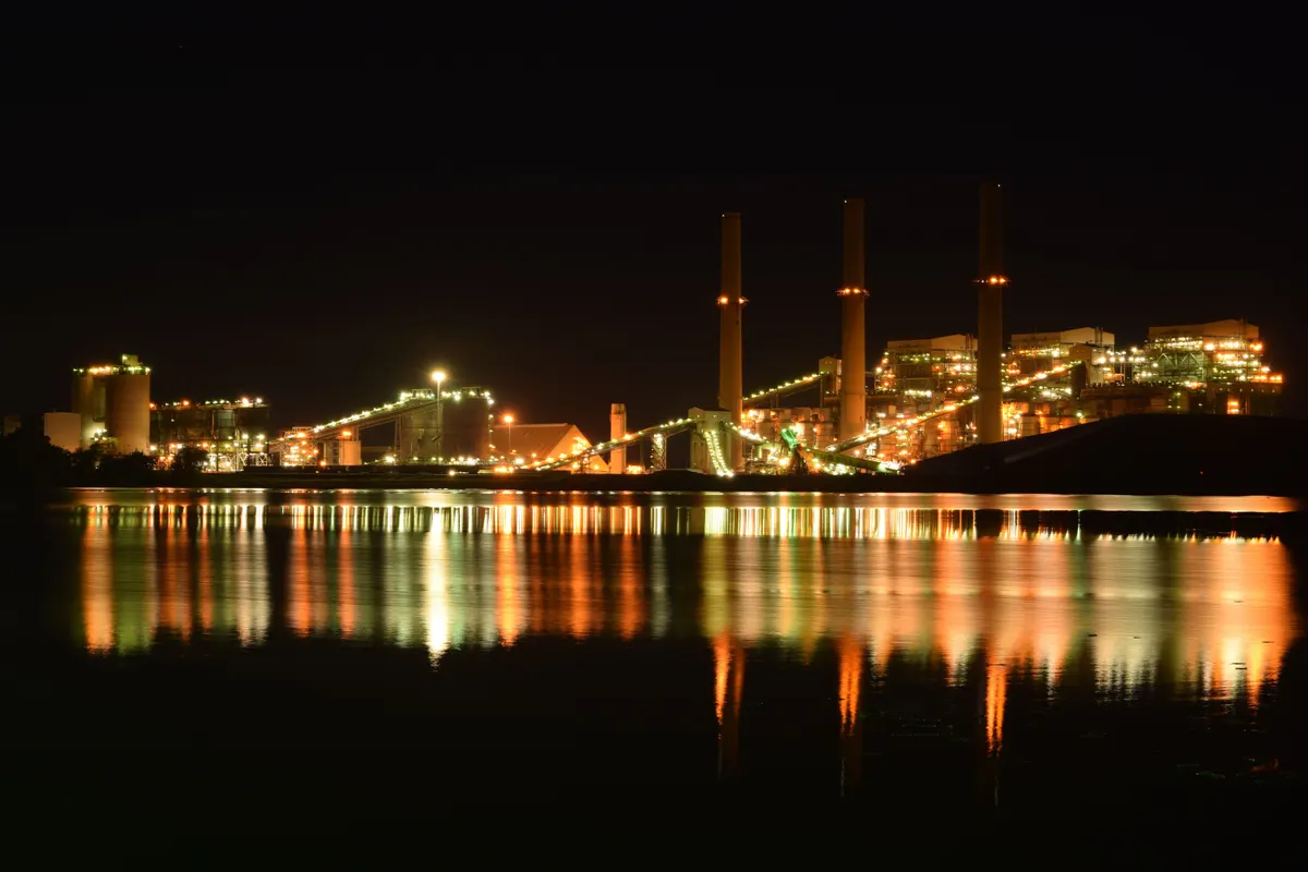 Planta industrial iluminada à noite, com as luzes refletidas na água em frente