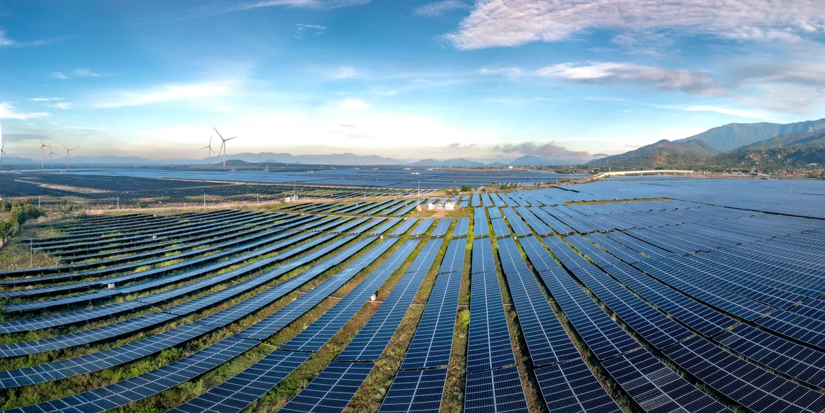 Vista aérea de usina solar com longas fileiras de painéis em terreno ondulado