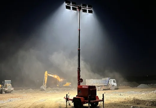 Torre de iluminação Revlo RV 4800 acesa em frente de lavra à noite, com escavadeira e caminhão basculante ao fundo