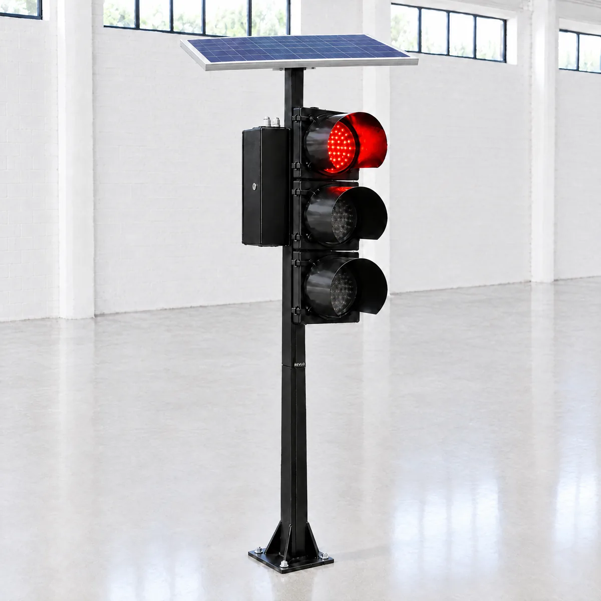Semáforo solar Revlo em coluna chumbada no piso de um galpão, com o painel solar nivelado no topo, o gabinete ao lado e o foco vermelho aceso